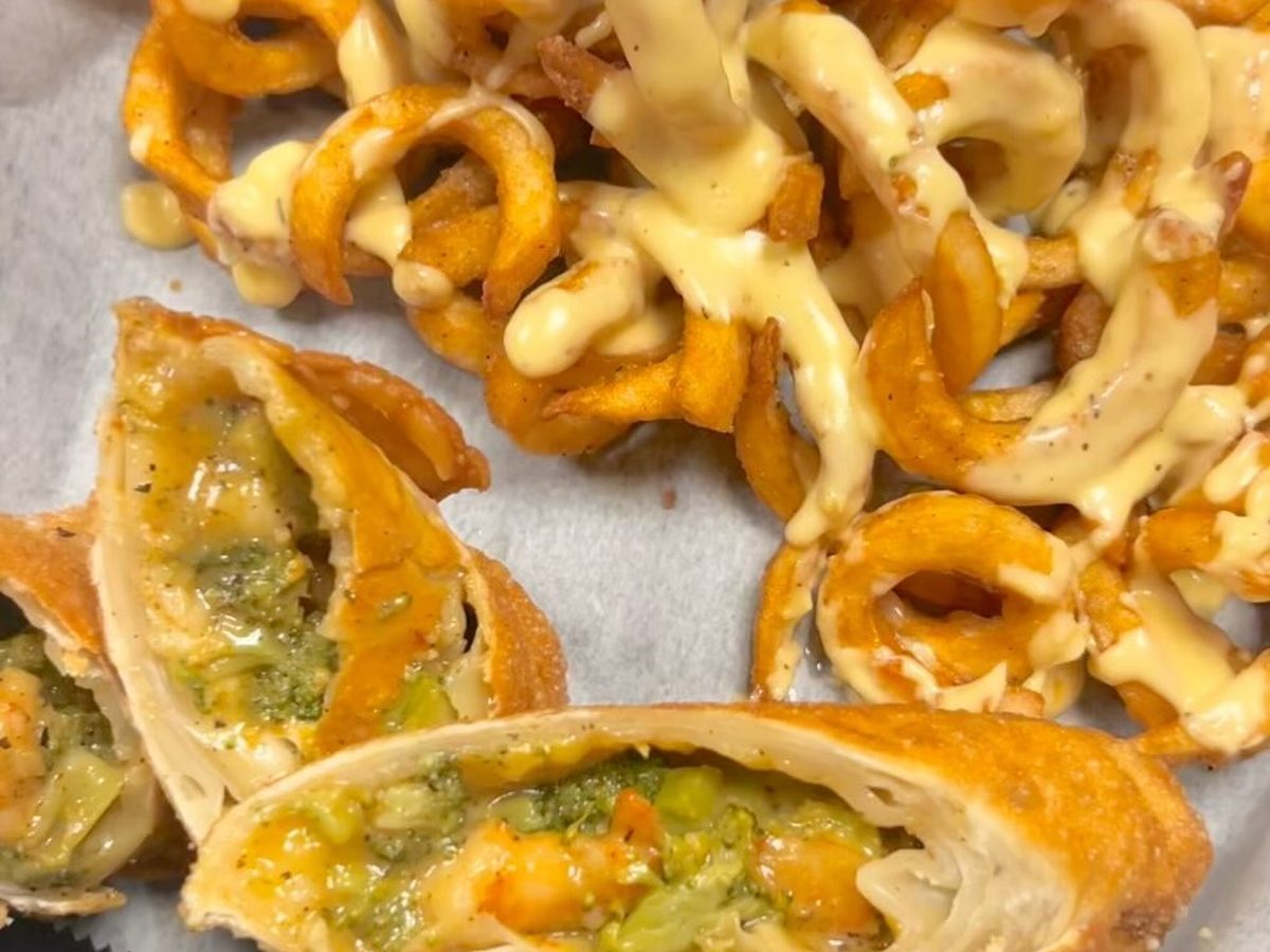 Shrimp and broccoli egg rolls cut open beside curly fries with cheese sauce