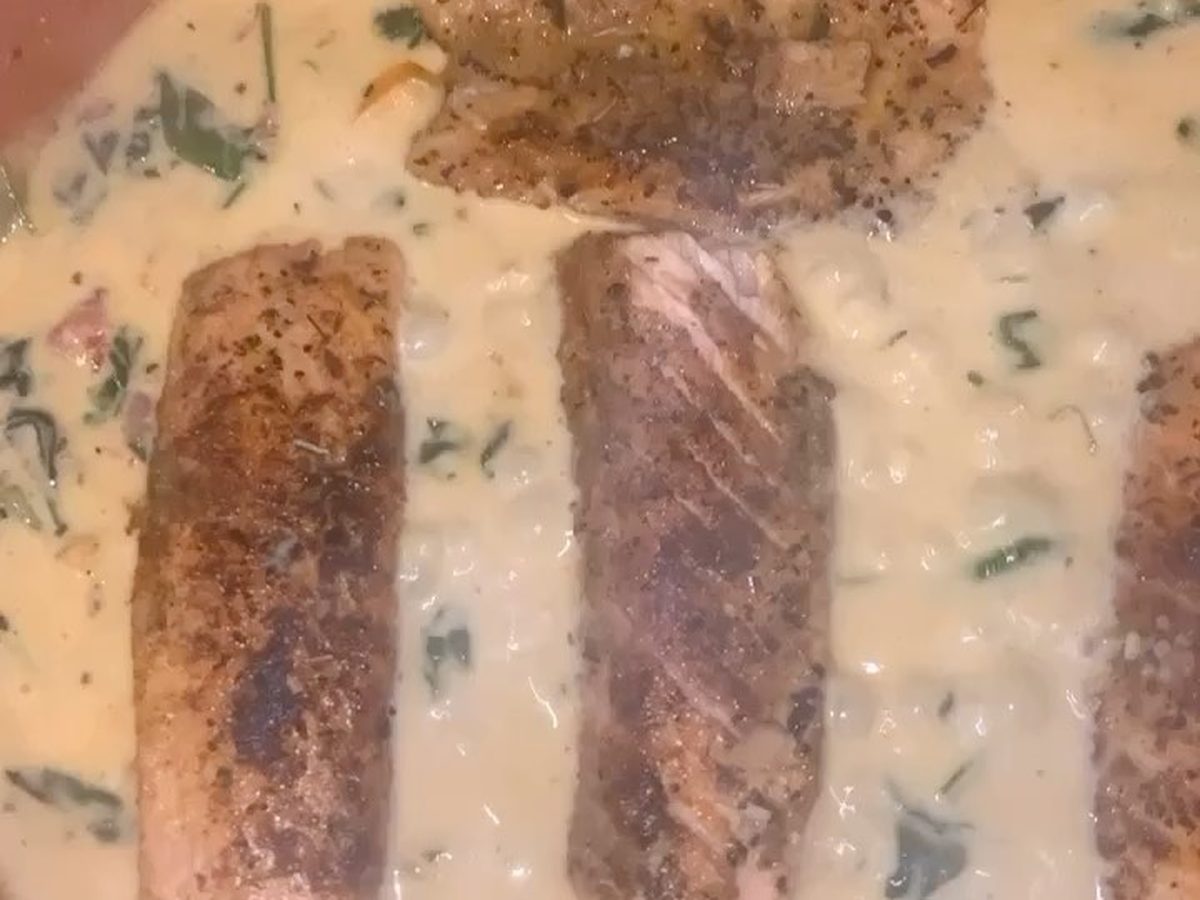 Two salmon fillets cooking in a cream sauce in a pan