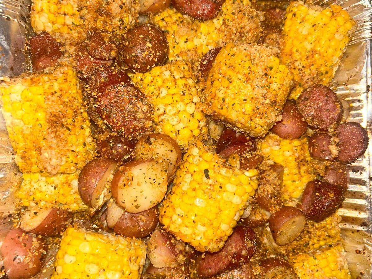 Corn on the cob, red potatoes and sliced sausage in seasoned butter in a foil tray