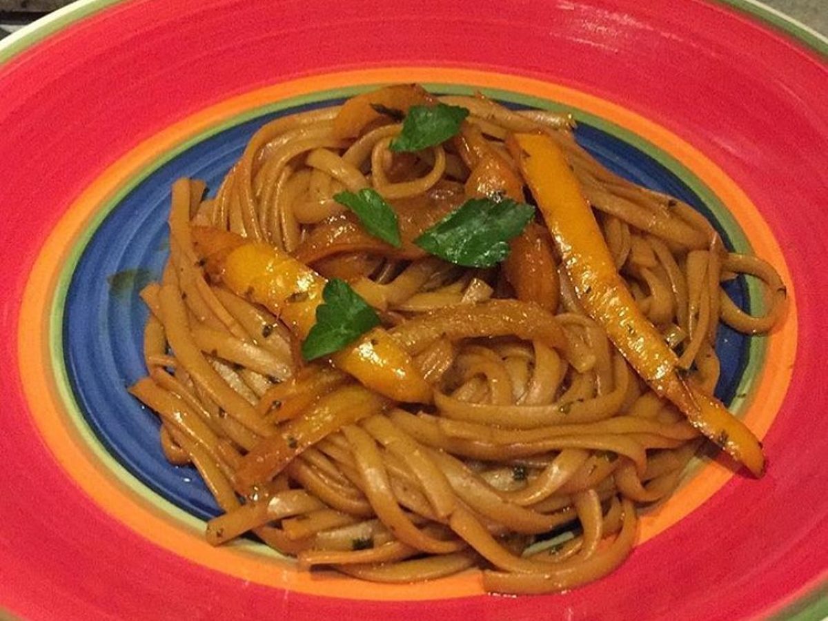 Noodles in brown sauce with sliced steak and peppers on a red plate